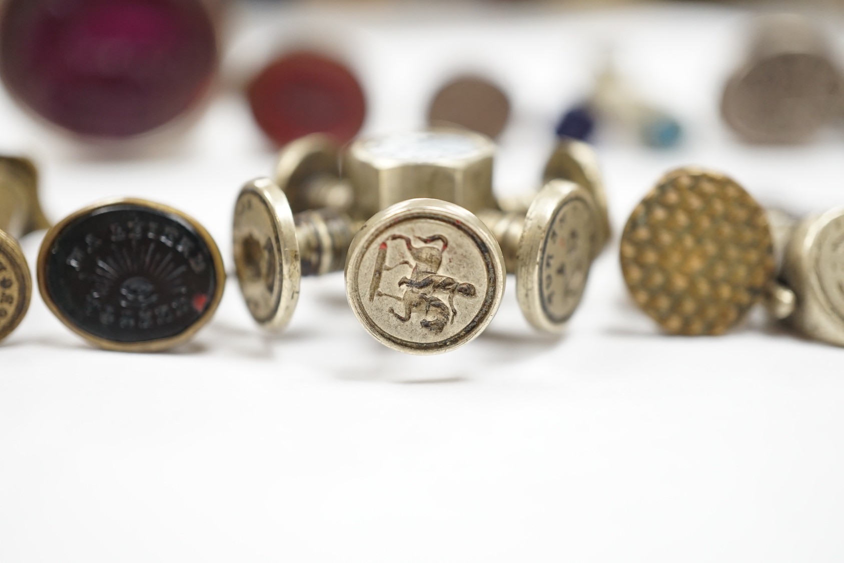 A group of twenty-five steel, gilt metal or nickel fob or desk seals, mostly 19th-century, including a steel swivel seal, a seal with boxwood finial modelled as a hand holding a ball and a nickel multi seal